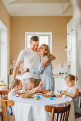 a happy family with three children is preparing for Easter in the kitchen at home, parents hug and smile, and children decorate colorful Easter eggs