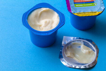 Fototapeta na wymiar Blue plastic containers with yogurt isolated on blue background - fun creamy yogurt image and selective focus