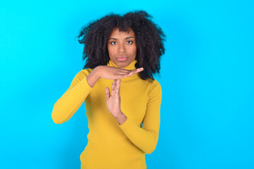 Fototapeta na wymiar Young woman with afro hairstyle wearing yellow turtleneck over blue background being upset showing a timeout gesture, needs stop, asks time for rest after hard work, demonstrates break hand sign