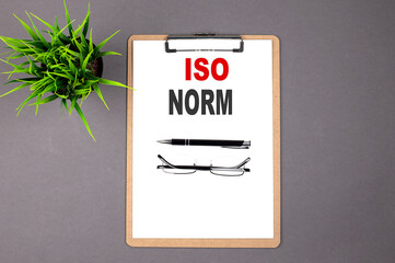 ISO NORM on the brown clipboard on the grey background. Business concept