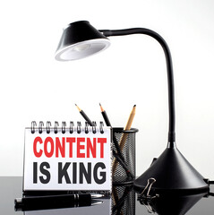 CONTENT IS KING text on notebook with pen and table lamp on the black background