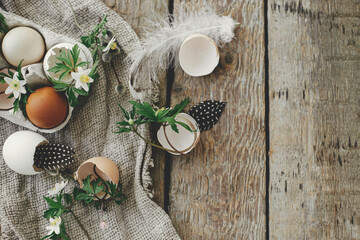 Easter rustic still life. Natural easter eggs, blooming spring flowers, feathers, burlap on rural wooden table. Happy Easter! Simple stylish festive decoration on table. Flat lay with space for text