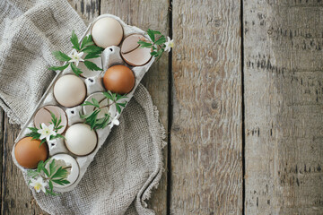 Easter rustic flat lay. Natural easter eggs with blooming spring flowers in tray on rural wooden table. Happy Easter! Simple stylish festive decoration on table. Flat lay with space for text