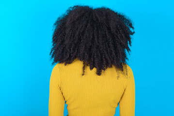 Fototapeta na wymiar The back view of a Young woman with afro hairstyle wearing yellow turtleneck over blue background . Studio Shoot.