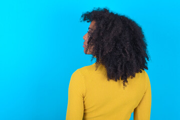 Fototapeta na wymiar The back side view of a Young woman with afro hairstyle wearing yellow turtleneck over blue background . Studio Shoot.