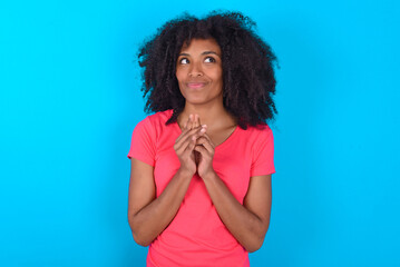 Young girl with afro hairstyle wearing pink t-shirt over blue background steepled fingers and looks...