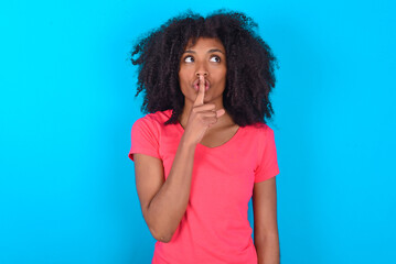Young girl with afro hairstyle wearing pink t-shirt over blue background  silence gesture keeps...
