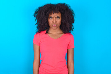 Offended dissatisfied Young girl with afro hairstyle wearing pink t-shirt over blue background with moody displeased expression at camera being disappointed by something