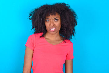 Portrait of dissatisfied Young girl with afro hairstyle wearing pink t-shirt over blue background...