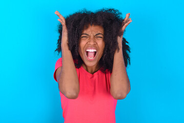 Young girl with afro hairstyle wearing pink t-shirt over blue background goes crazy as head goes...