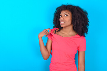 Young girl with afro hairstyle wearing pink t-shirt over blue background stressed, anxious, tired and frustrated, pulling shirt neck, looking frustrated with problem