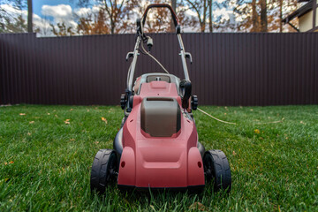 Red electric lawn mower on a green lawn. Selective focus.