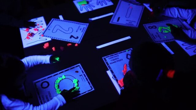 Unrecognizable children in ASD class doing a plastic class activity with black lights and phosphorescent colors pictograms