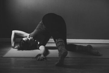 Grayscale shot of a young female practicing yin yoga in a studio
