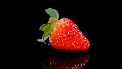 Strawberry on a black background close up view. Fresh, organic vibrant red strawberry. Raw vegan summer snack.