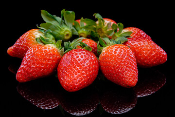 Strawberries on a black background close up view. Fresh, organic vibrant red strawberry. Raw vegan summer snack.