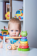 Handsome toddler boy playing with educational wooden and plastic toys in children's room..