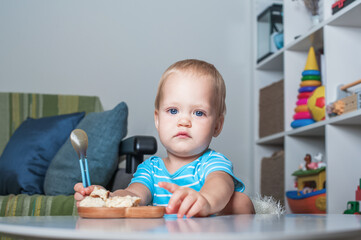 Toddler boy eats on his own at table at home..