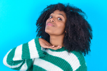 Young woman with afro hairstyle wearing striped sweater over blue background cutting throat with...