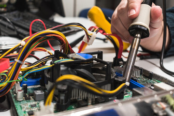 IT technician soldering a part of a computer motherboard in an office