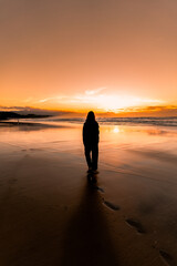 Naklejka premium Girl walking barefoot on a beach at sunset