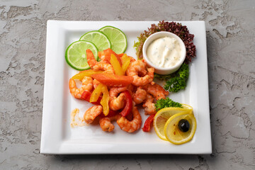 Shrimps fried with vegetables on white plate with sauce