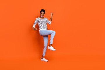 Fototapeta na wymiar Photo of excited lucky third gender person wear pullover rising fists walking empty space isolated orange color background