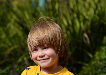 Positive kid, three years old. Portrait of a boy on a background of yellow flowers. Close-up.