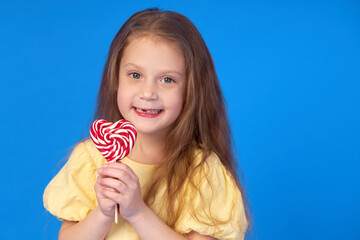 Toothless child. Cute little girl smiles broadly with lollipop  in hands. The first milk tooth fell...