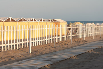 Footpath on the beach and yellowish tents in the background with sunset light