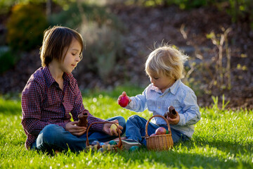 Cute children, eating chocolate bunnies and fighting with easter eggs after egg hunting in garden