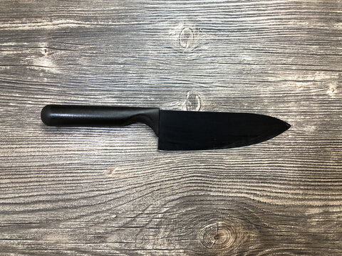 The black knife lying on the table with wooden texture.