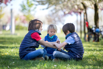 Three children, boy brothers, playing rock scissors paper game in park