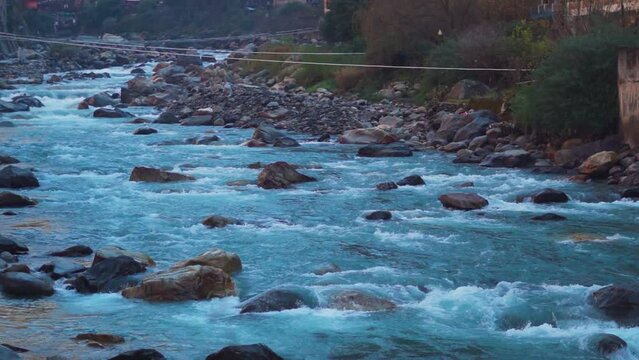 Slow motion shot of the Paravti River flowing in between mountains at Kasol in Himachal Pradesh, India. View of the Parvati river during the winter. Natural river in the mountains background.	