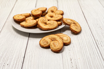 Palmier puff pastry biscuits in white plate on a white painted wooden table