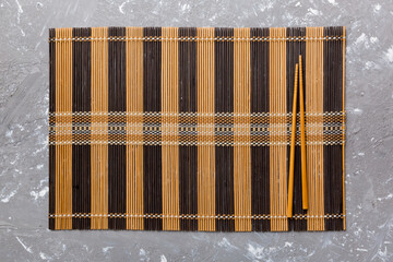 Two chopsticks and bamboo mat on cement background. Top view, copy space