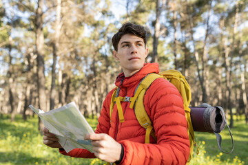 Young caucasian traveler standing in the forest looking at the lost map. Travel and active lifestyle concept, trekking