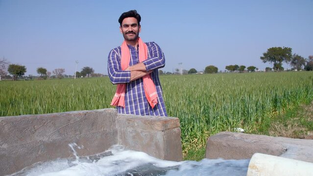 A confident bearded farmer standing near a tubewell with his folded arms - leisure time  relaxation. A happy worker / laborer in casual clothes and wearing a Safa posing for the camera in his green...
