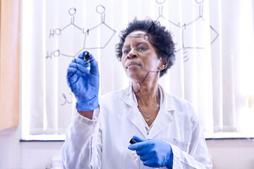 Testing some of her ideas. Shot of a female scientist drawing molecular structures on a glass wall...