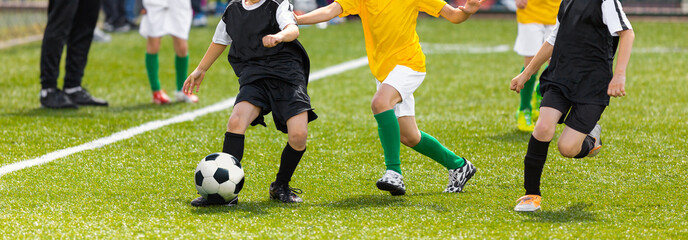Obraz premium Horizontal image of soccer kids kicking ball on school stadium. Elementary age children play sports. Group of boys in football uniforms compete in tournament match