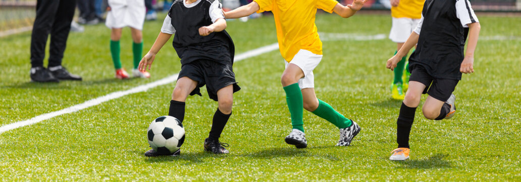 Horizontal image of soccer kids kicking ball on school stadium. Elementary age children play sports. Group of boys in football uniforms compete in tournament match