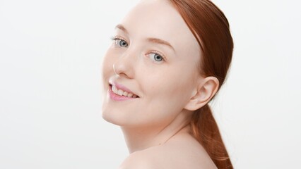 Attractive young ginger woman looks at the camera over her shoulder smiling widely on white background | Cosmetic product commercial concept