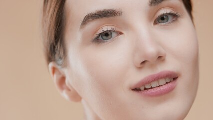 Fototapeta premium Txtreme close-up beauty portrait of young cute European woman with dark hair looking at camera against beige background | Face care concept