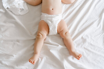 legs of a six month old baby in diapers lying on a bed at home