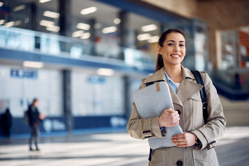 Fototapeta premium Portrait of happy businesswoman with laptop at airport terminal looking at camera.