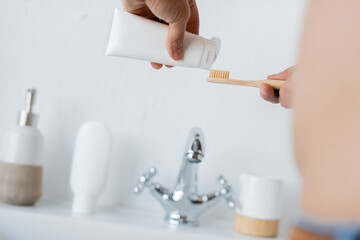 Fototapeta na wymiar cropped view of man squeezing toothpaste on toothbrush in bathroom.