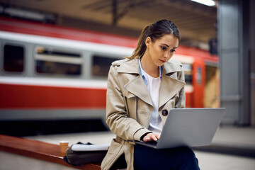 Young woman works on laptop while waiting at train station.