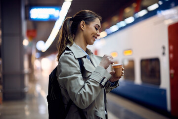 Happy woman enjoys in takeaway coffee at train station.