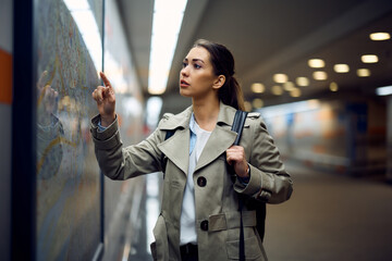 Female passenger checking public transport map while waiting for train at subway.