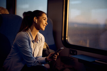 Fototapeta Young happy woman looks through window while traveling by train at sunset. obraz
